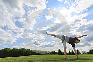 Man stretching hands and legs on green grass in park. Yoga and healthy lifestyle concept