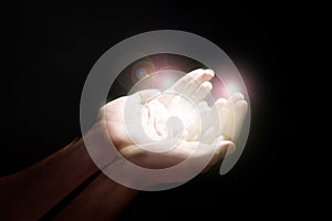 Man stretching hands towards light in darkness, closeup. Praying concept