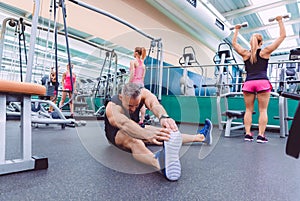 Man stretching and women doing dumbbells exercises in gym