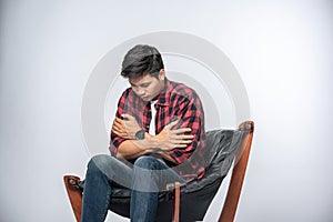 The man in a striped shirt sits sick and sits on a chair and crosses his arms