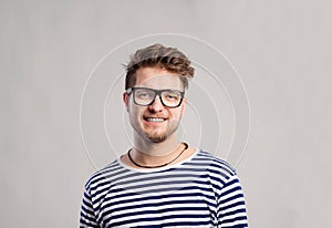 Man in striped t-shirt and eyeglasses against gray background.