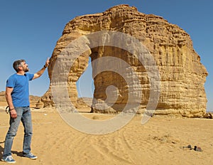 A man stroking the rock formation known as the Elephant Rock in Al Ula, Saudi Arabi KSA