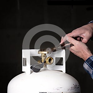 Man struggles with pliers on a propane tank