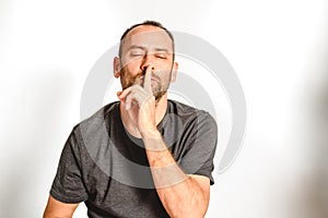 Man in studio asking for silence with a wave of his hand putting a finger on his lips, model expressions isolating white