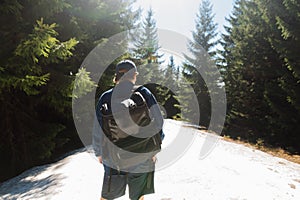 Man in stylish casual clothes with a backpack on his back standing in the mountains in the snow on a background of coniferous