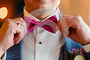 A man in a stylish suit corrects a pink butterfly. Closeup of a corporate man adjusting his fashionable pink tie. Business concept