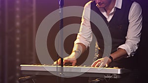 Man in stylish suit and original glasses plays of synthesizer near retro microphone. The musician touches the keys with