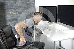 Man suffering from backache while sitting at computer desk in office