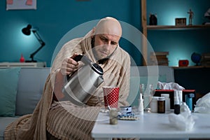 A man suffering from a cold and high fever pours tea into a cup. Flu treatment concept at home