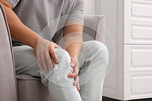 Man suffering from knee pain on armchair indoors, closeup
