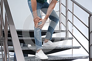 Man suffering from knee pain while going downstairs indoors. Health problems