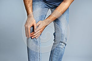 Man suffering from knee pain on grey background