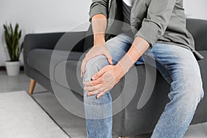 Man suffering from knee pain at home, closeup. Space for text