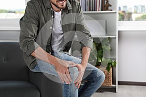 Man suffering from knee pain on sofa at home, closeup