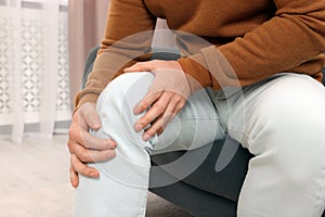 Man suffering from knee pain on sofa indoors, closeup