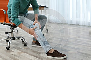 Man suffering from leg pain indoors with space for text