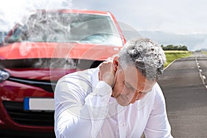 Man Suffering From Neck Pain In Front Of Breakdown Car