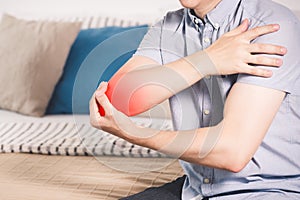 Man suffering from pain in elbow at home, joint inflammation