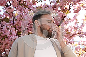 Man suffering from seasonal pollen allergy near blossoming tree outdoors