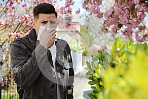 Man suffering from pollen allergy near blossoming tree outdoors