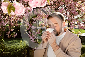 Man suffering from seasonal pollen allergy near blossoming tree outdoors