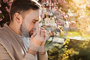 Man suffering from seasonal pollen allergy near blossoming tree outdoors