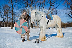 Man in suit of ancient warrior standing near the big white horse