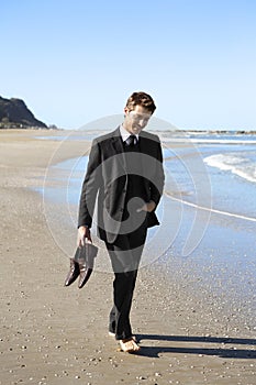 Man in suit barefoot on beach holding shoes