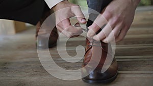 Man in suit and black socks ties his shoelaces into bow on brown shoes on floor.