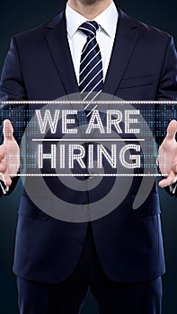 Man in suit, digital banner WE ARE HIRING, dark background, formal attire photo