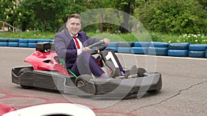 Man in a suit driving Go-Kart car in a playground.