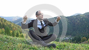 A Man In A Suit And Glasses Is Sitting Cross-legged In The Mountains And Cannot Hide His Joy