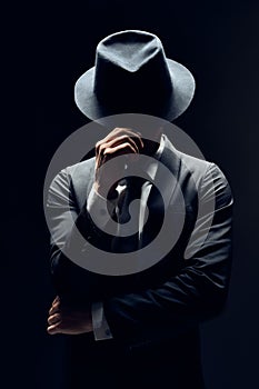 Man in suit hiding face behind his hat isolated on dark background