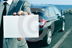 man in suit holding a blank signboard with a car in the background