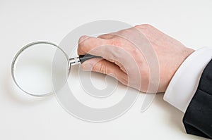 Man in suit holds magnifying glass. Isolated on white background