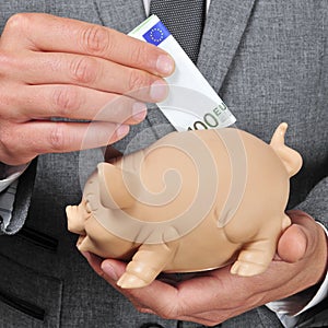 Man in suit introducing a euro bill in a piggy bank