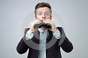 Man in suit looking through binoculars with shock and wonder