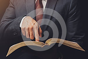 man in suit pointing a text on an open bible on a black background