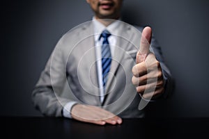 Man in suit showing thumbs up, businessman making a great gesture in a dark room.