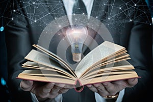 A man in a suit shows an open textbook and a burning light bulb