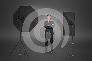 Man in suit standing with arms folded in studio with reflectors on both sides.