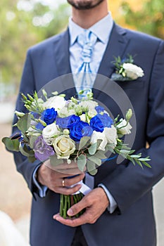 Man in suit and stylish tie is holding wedding bouquet