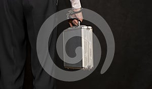 A man in a suit with a suitcase handcuffed on a black background, close-up, selective focus, dark tonality. Concept: secure delive