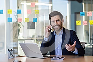 A man in a suit is talking on his cell phone while sitting at a desk