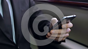 Man in suit texting e-mail on his smart phone while sitting on car back seat