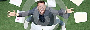 Man in suit throwing papers on green grass and yelling with his hands up top view