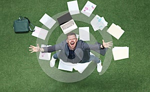 Man in suit throwing papers on green grass and yelling with his hands up top view