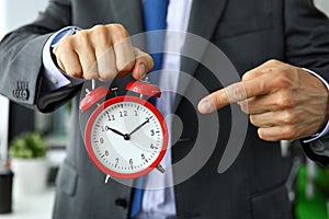 Man in suit and tie point finger to red vintage alarm clock face