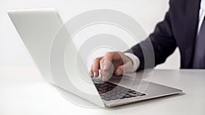 Man in suit typing on laptop in office, pushing spacebar, online working concept photo