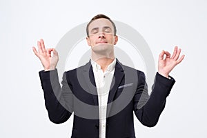 Man in suit and white shirt standing, raised arms, closed eyes with yoga gesture and meditation